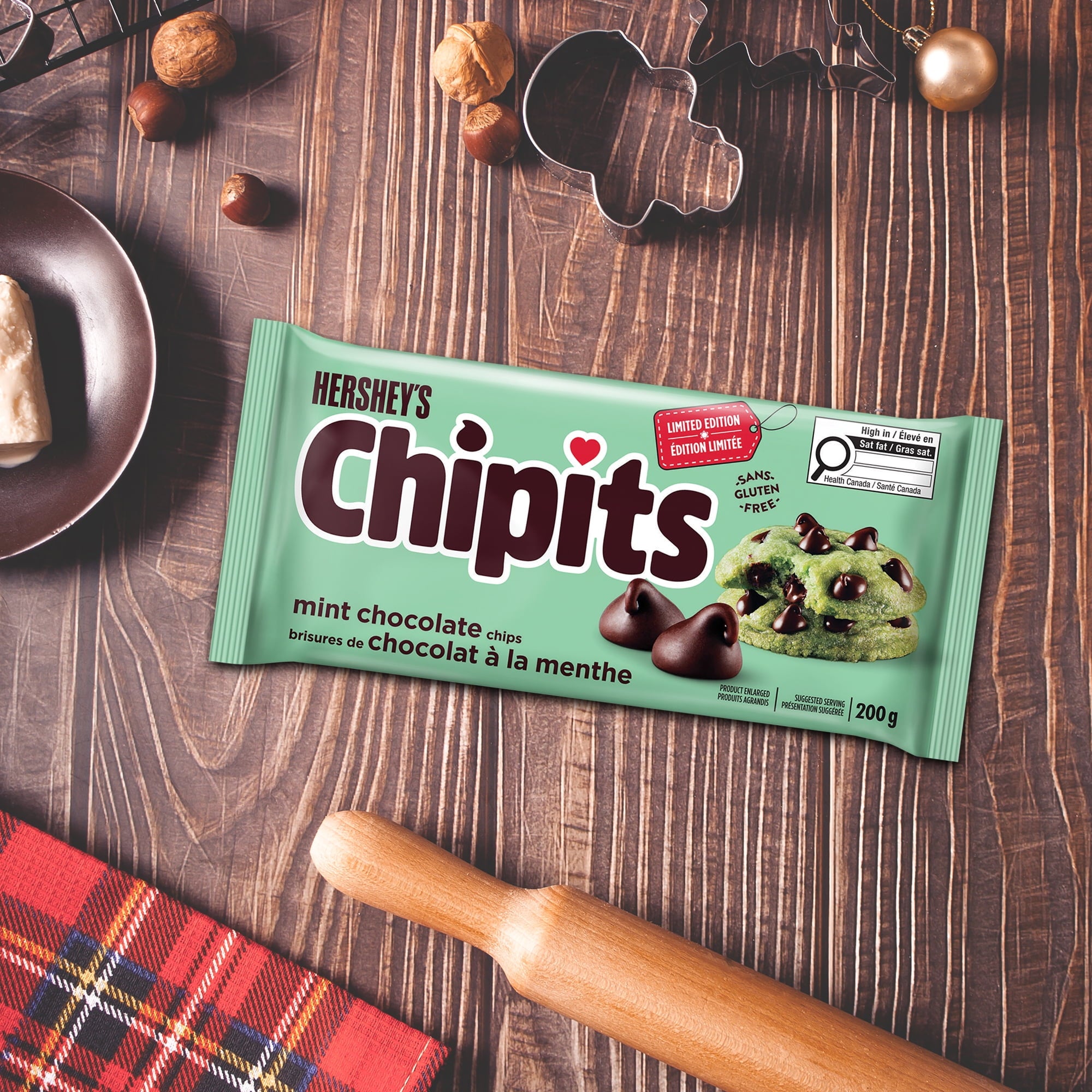 Hershey's Chipits mint chocolate chips packaging on a wooden surface with cookies and a rolling pin.