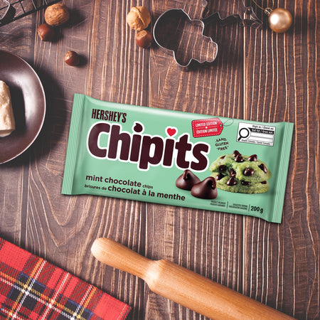 Hershey's Chipits mint chocolate chips packaging on a wooden surface with cookies and a rolling pin.