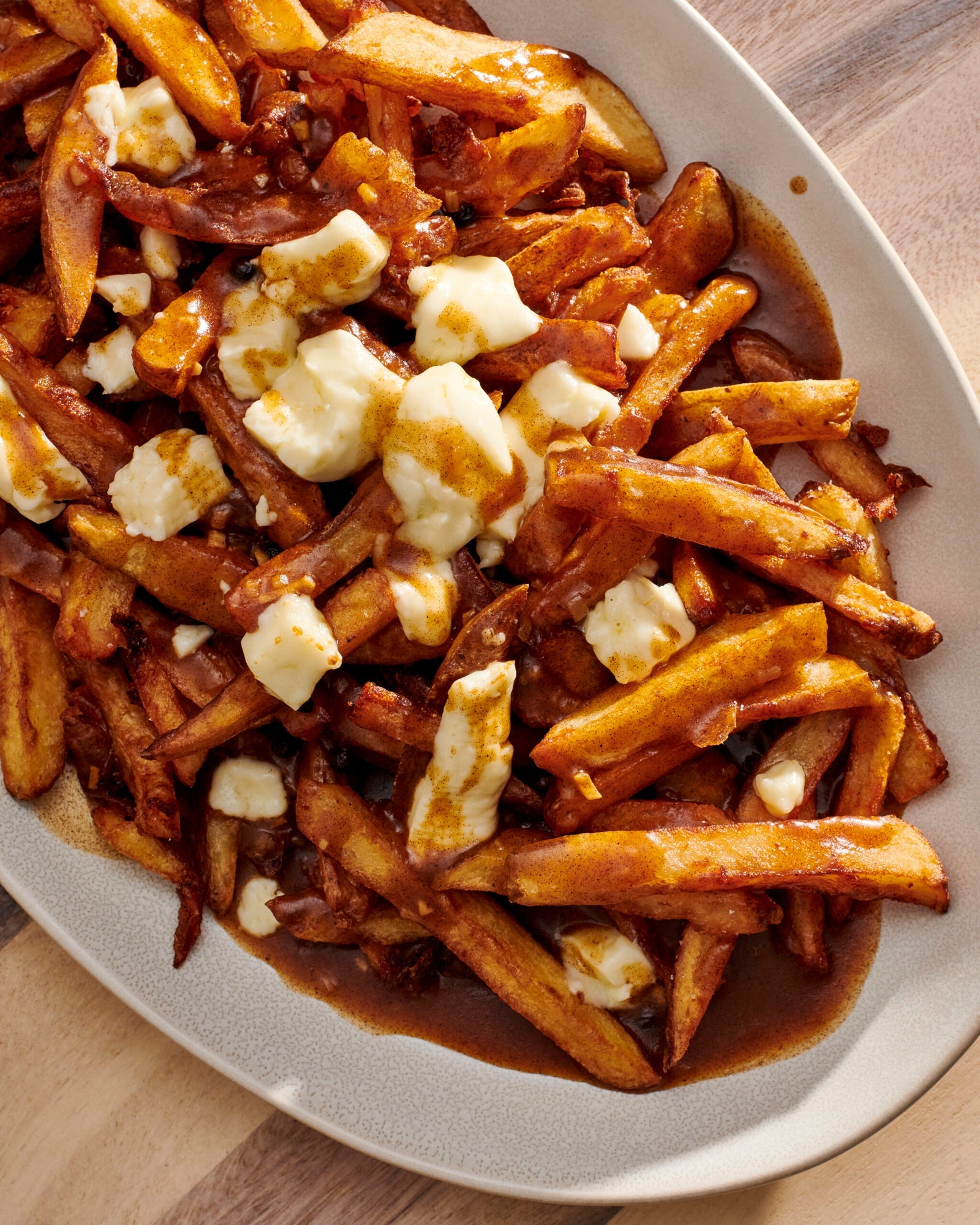 Platter of poutine with fries, gravy, and cheese curds on a wooden surface