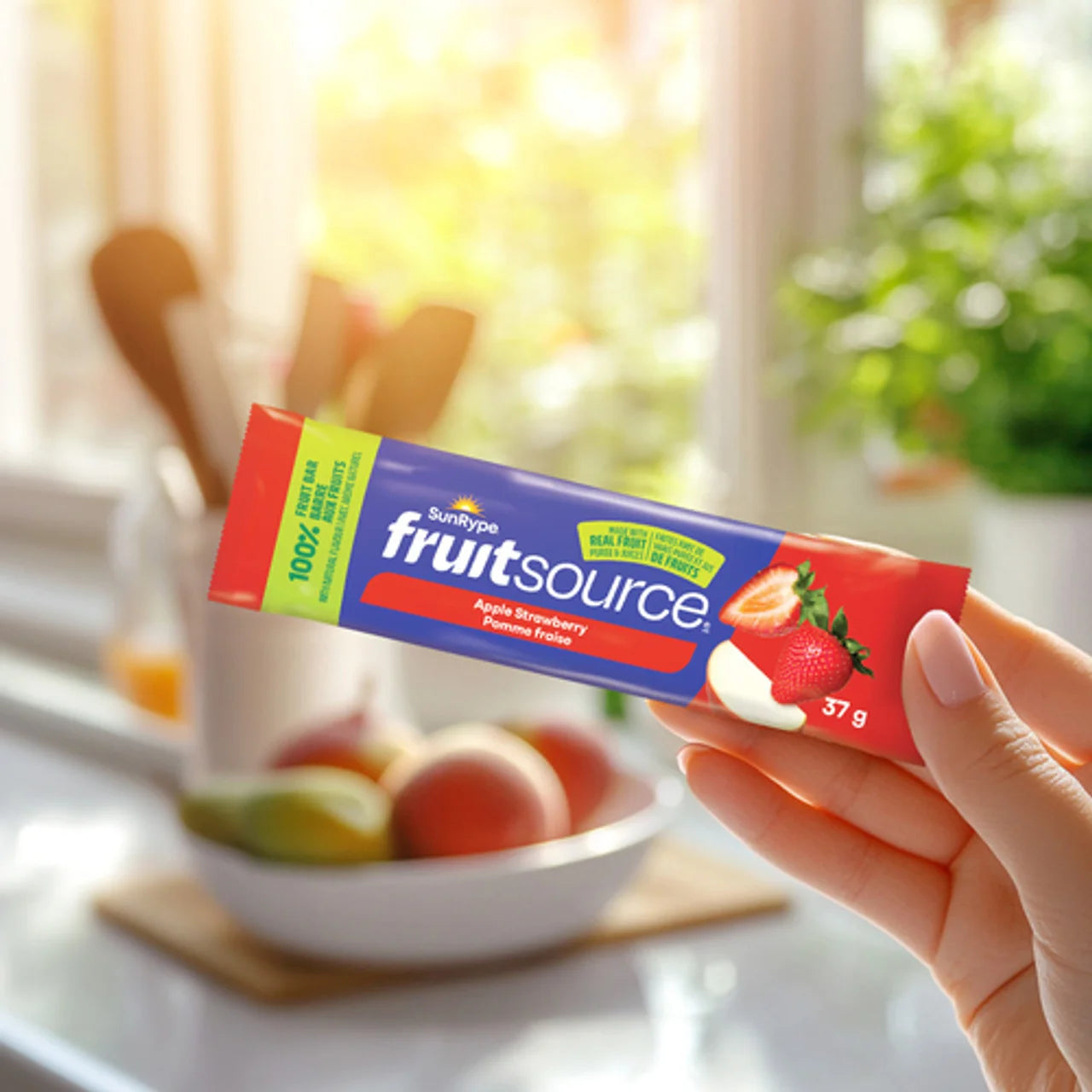 Hand holding a Sunripe Fruitsource fruit bar with a blurred kitchen background