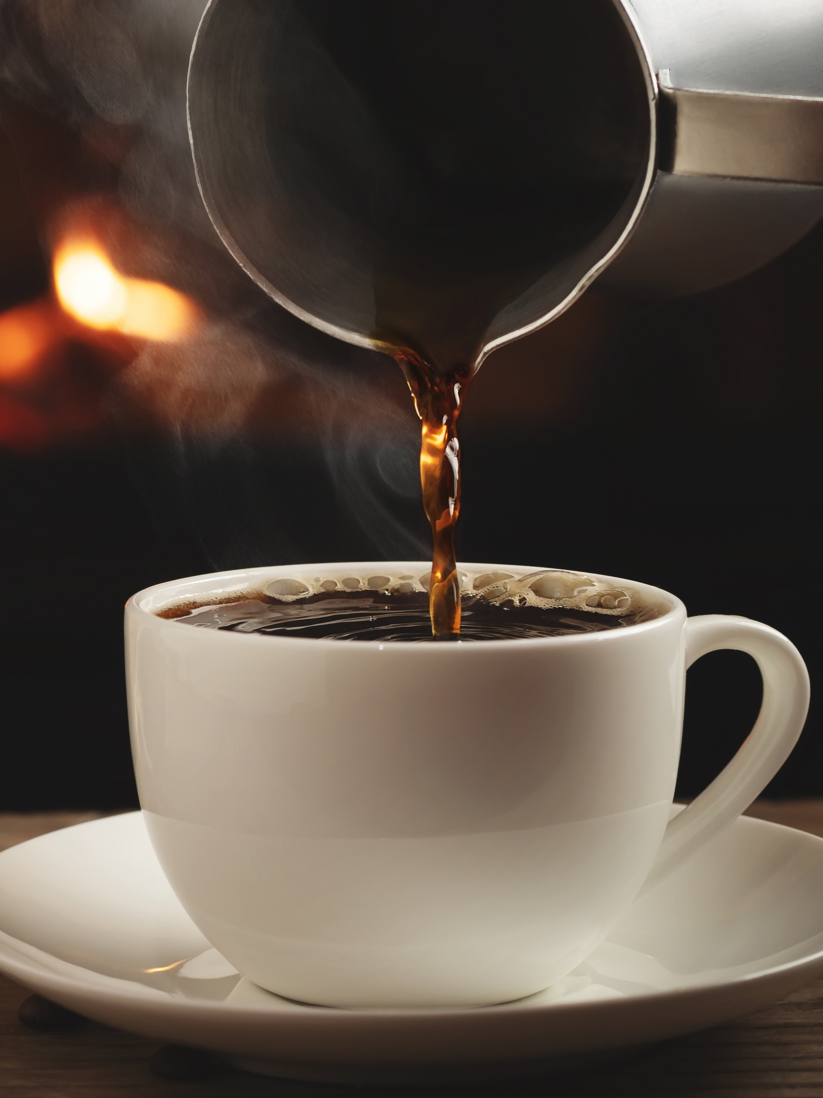 Steaming coffee being poured from a pot into a white cup on a dark background
