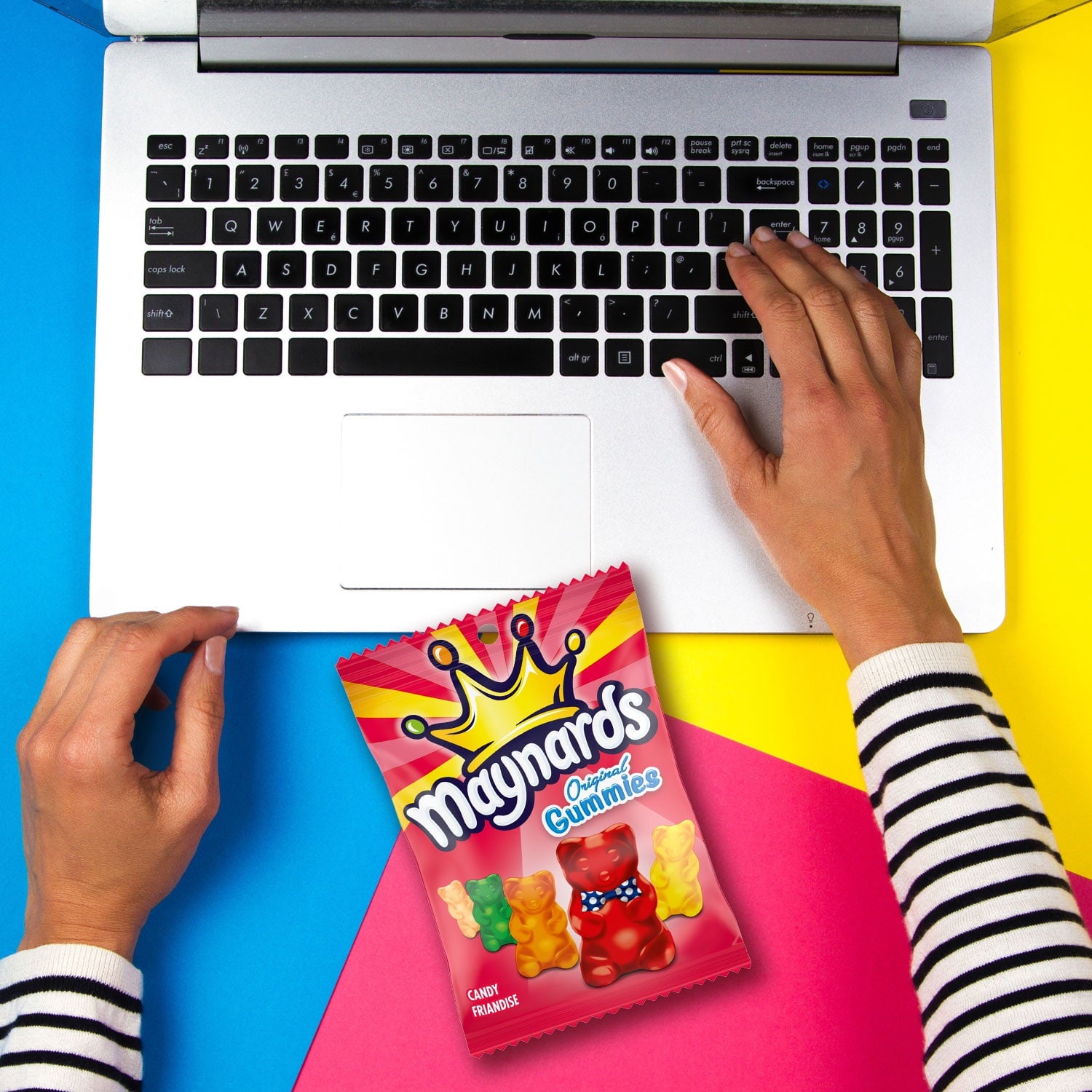 Person using a laptop with a Maynards gummy bears packet on a colorful background
