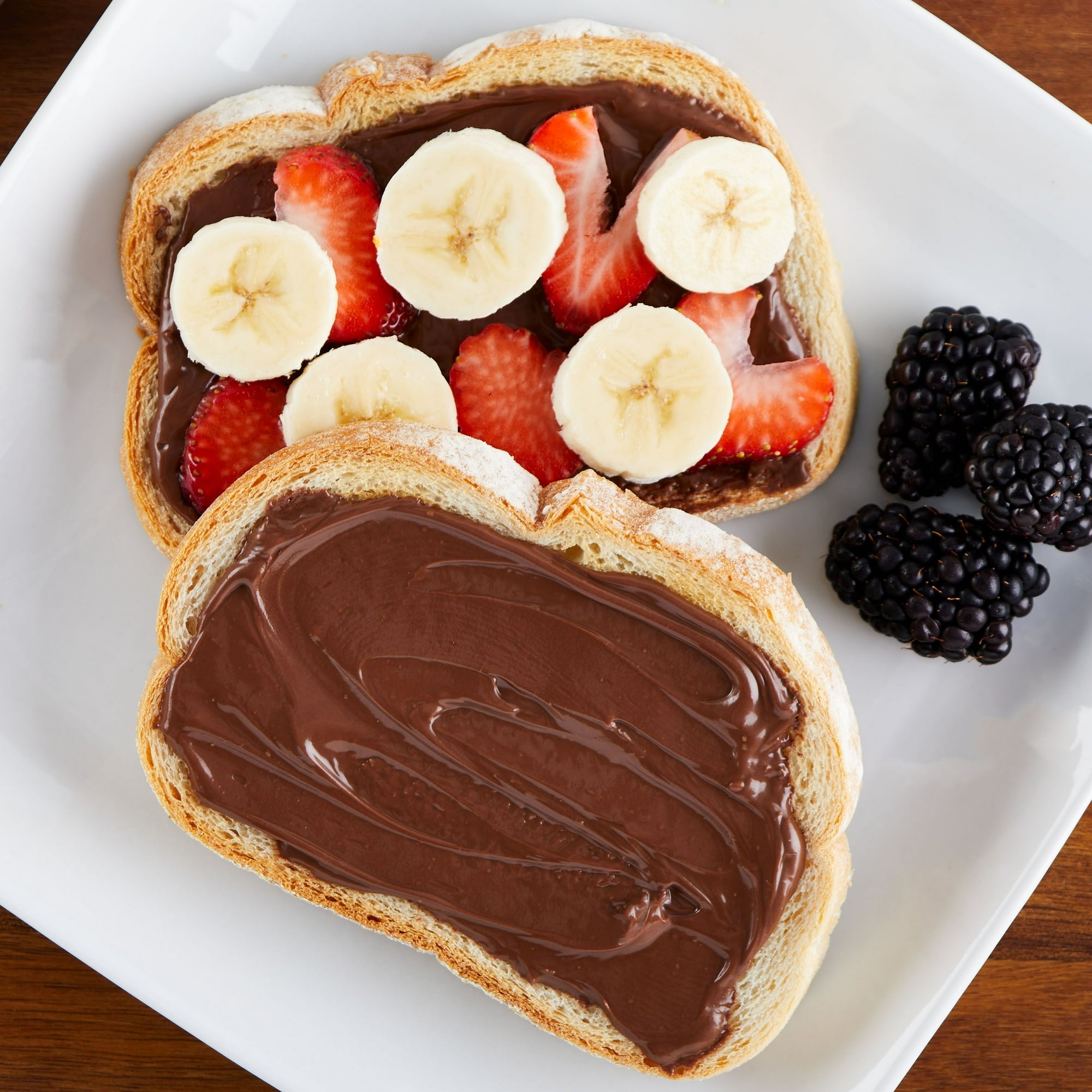 Great Value Hazelnut Spread with Cocoa, 375g/13.2 oz - Two slices of bread with chocolate spread, strawberries, and bananas on a white plate.