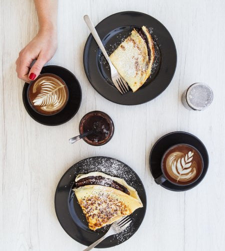Two cups of Lavazza Crema E Gusto coffee with crepes on a white wooden surface