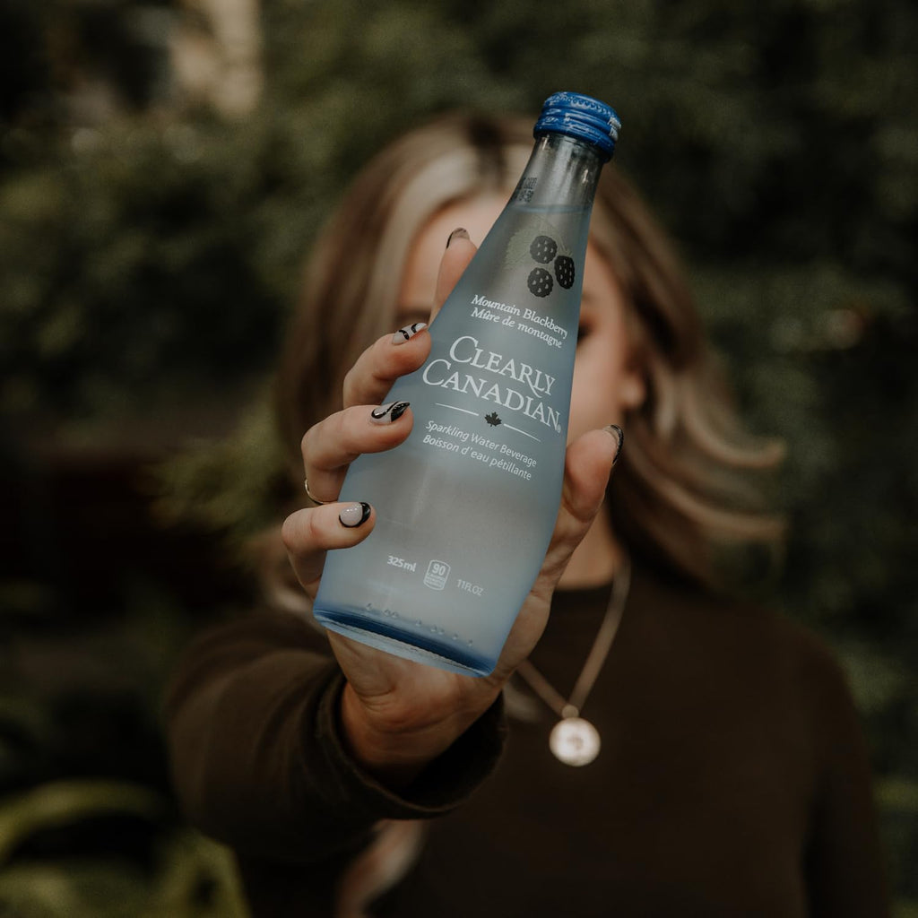 Clearly Canadian Sparkling Water Beverage, Mountain Blackberry, 325ml/11 Fl oz., Bottle, a person holding a bottle.