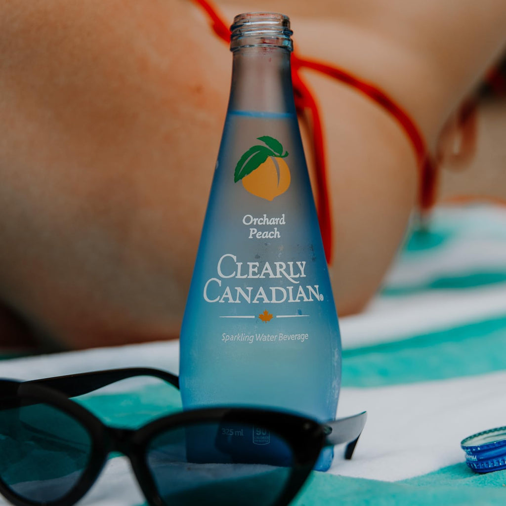 Clearly Canadian Sparkling Water Beverage, Orchard Peach, 325ml/11 Fl oz., Bottle, bottle on the beach.