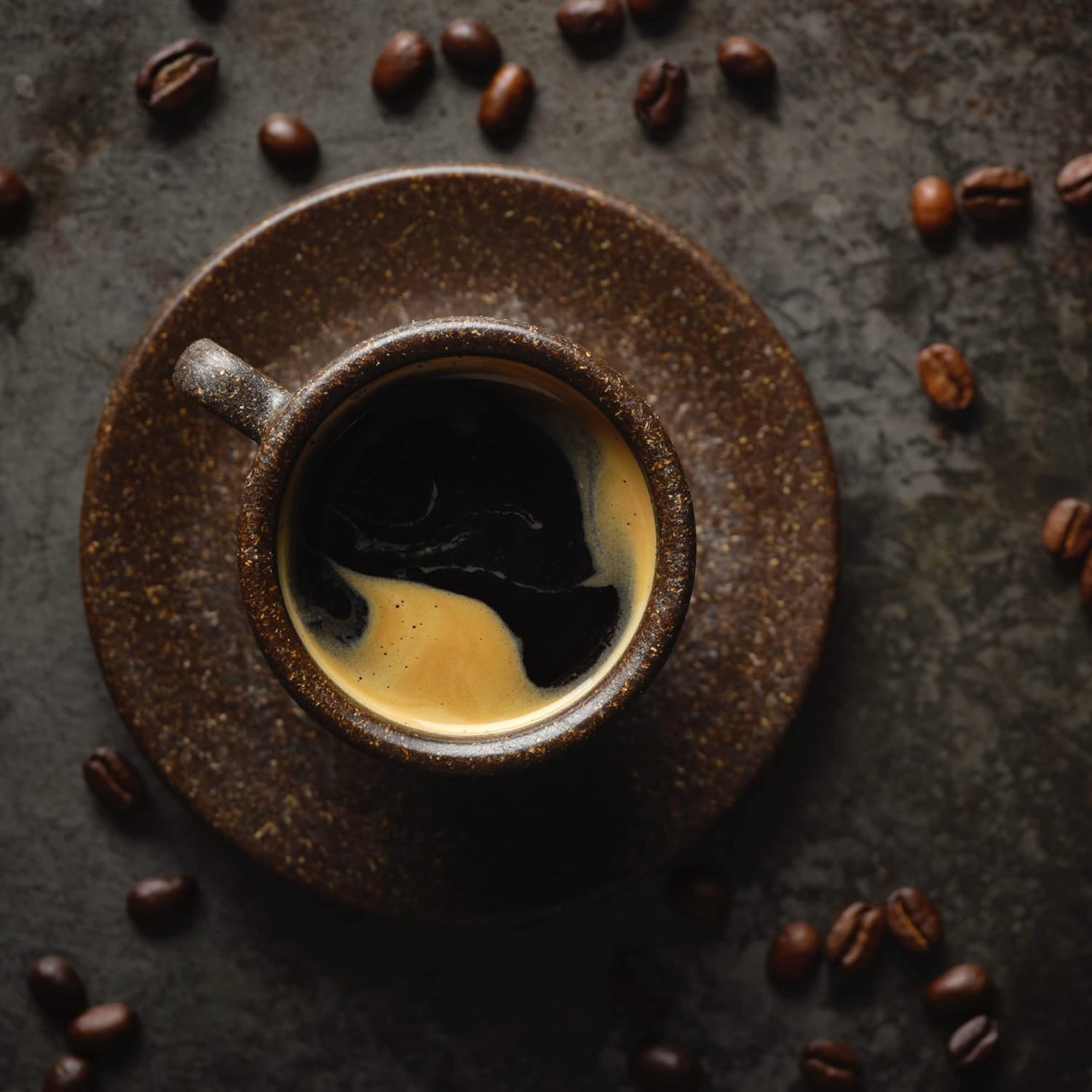 A cup of hot coffee on a dark brown marble surface with coffee beans scattered around it