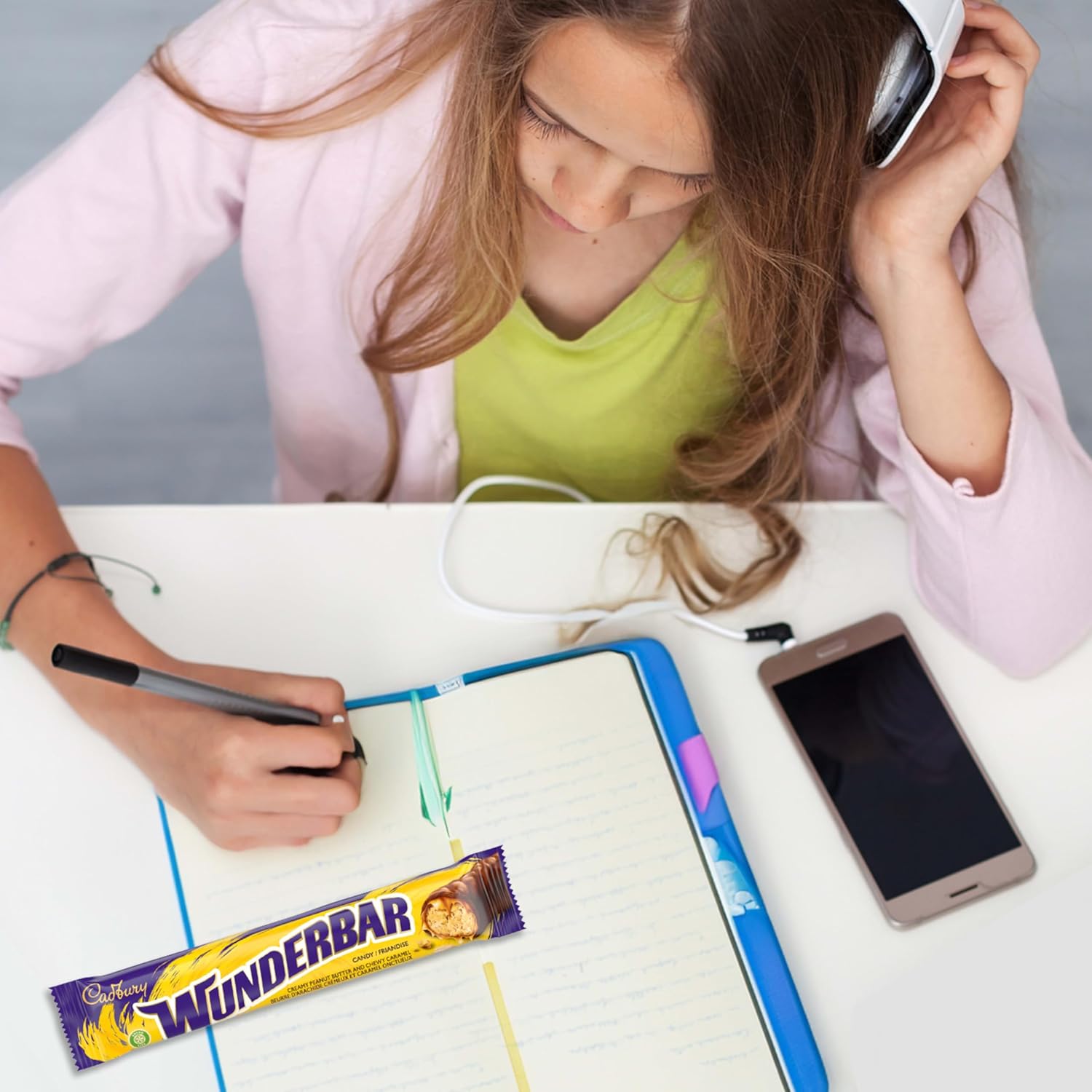 Child sitting at a table with a smartphone, notebook, and Cadbury Wunderbar bar.