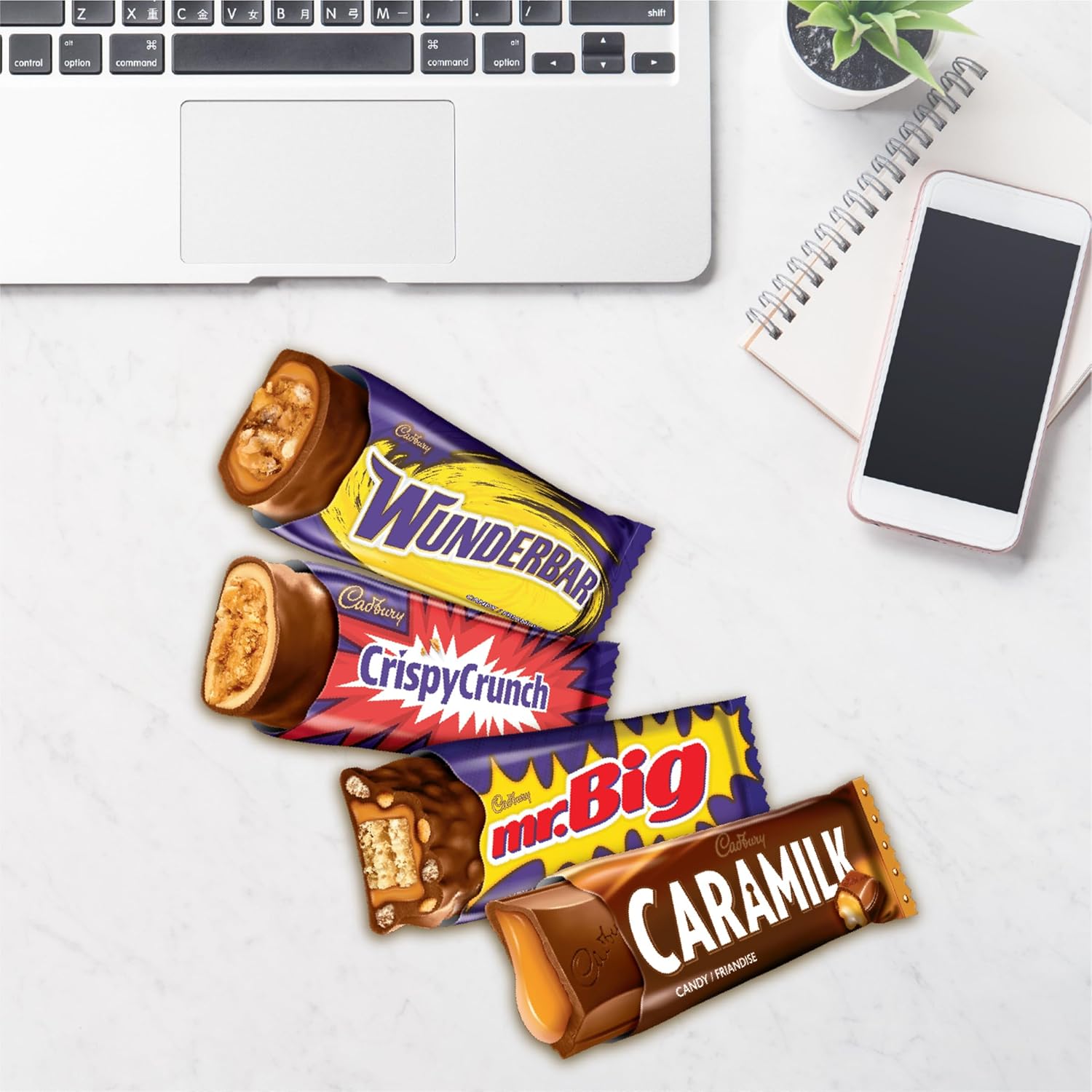 Candy bars from Cadbury on a desk with a laptop, phone, and plant.