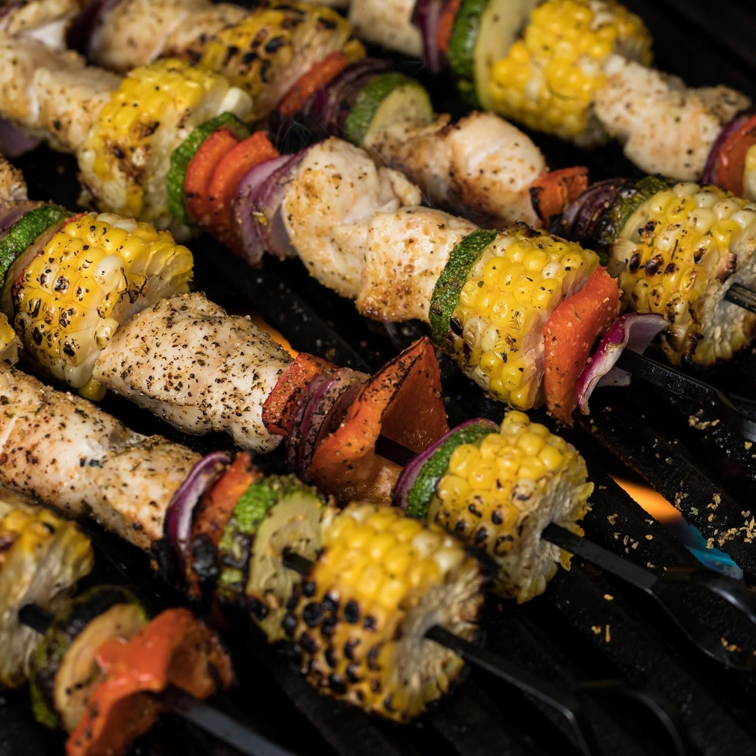 Close-up of skewers with chicken, corn, and vegetables on a grill.