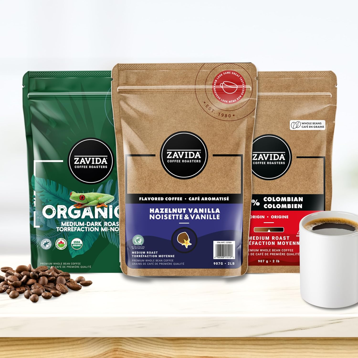 Three Zavida coffee packages with a cup of coffee and coffee beans on a white background