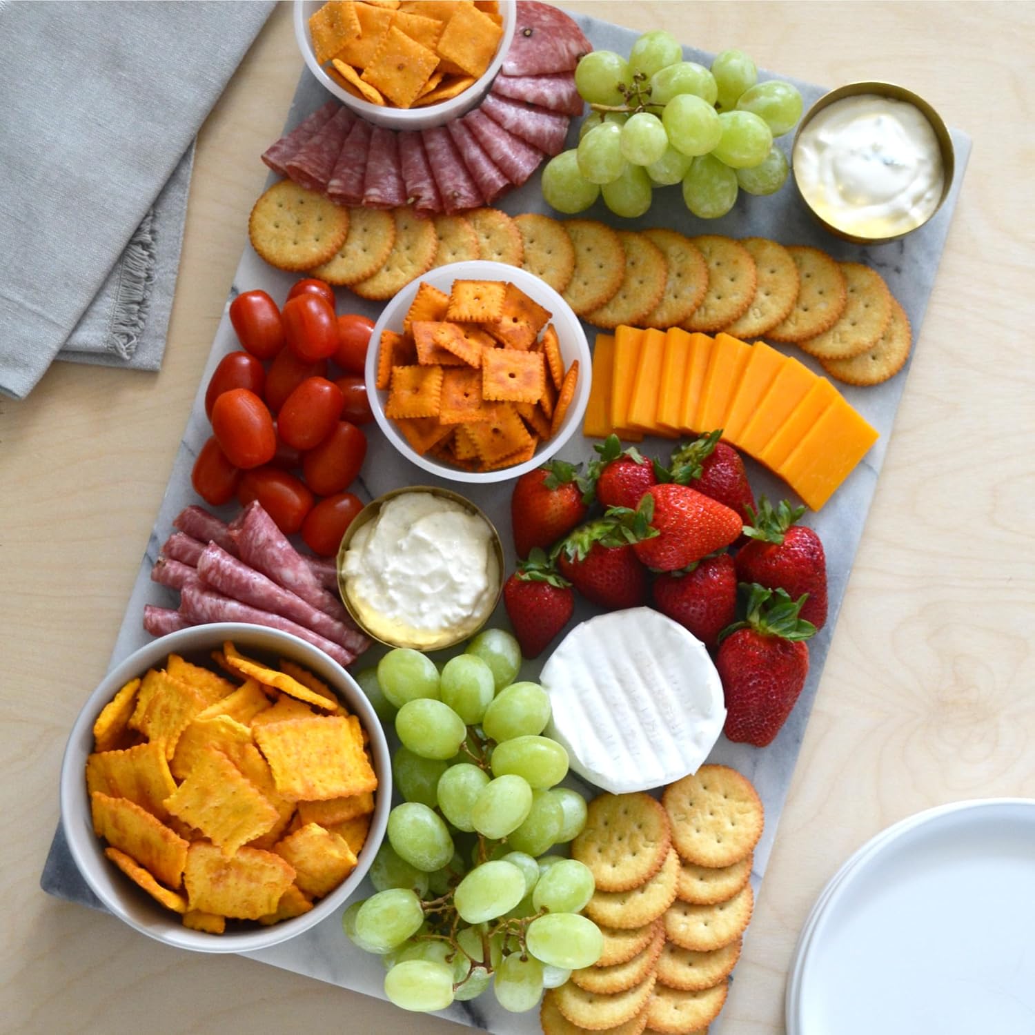 Platter of assorted snacks including crackers, cheese, fruits, and chips on a wooden surface.