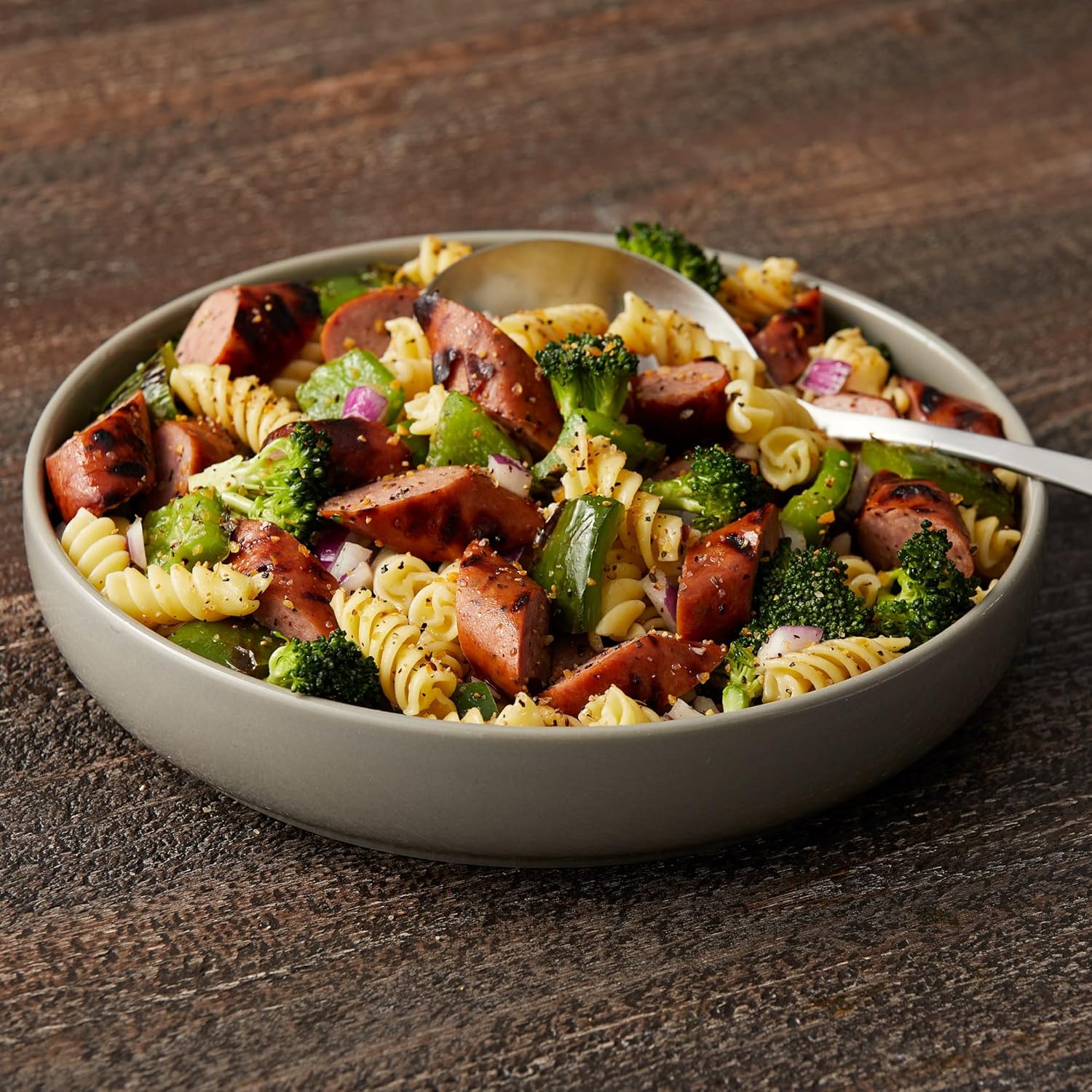 Pasta salad with sausages and broccoli in a bowl on a wooden surface