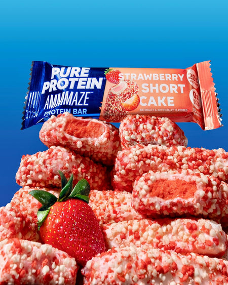 Stack of strawberry shortcake protein bars with a Pure Protein Ammamaze bar on a blue background