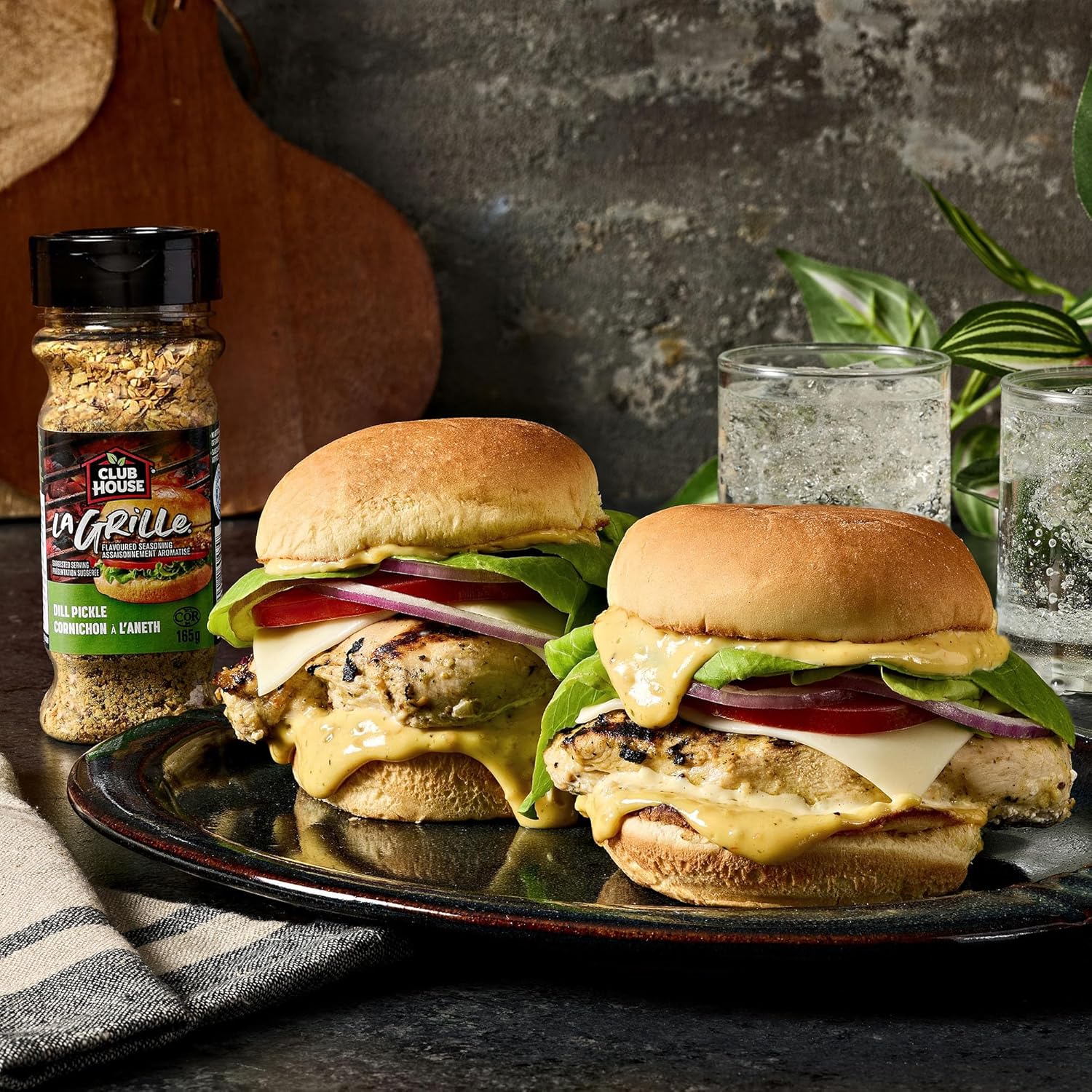 Two burgers on a plate with a bottle of Club House La Grille Dill Pickle Seasoning in the background.