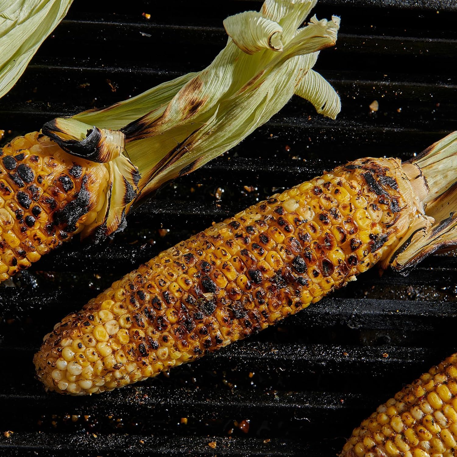Grilled corn on the cob with charred spots on a grill surface
