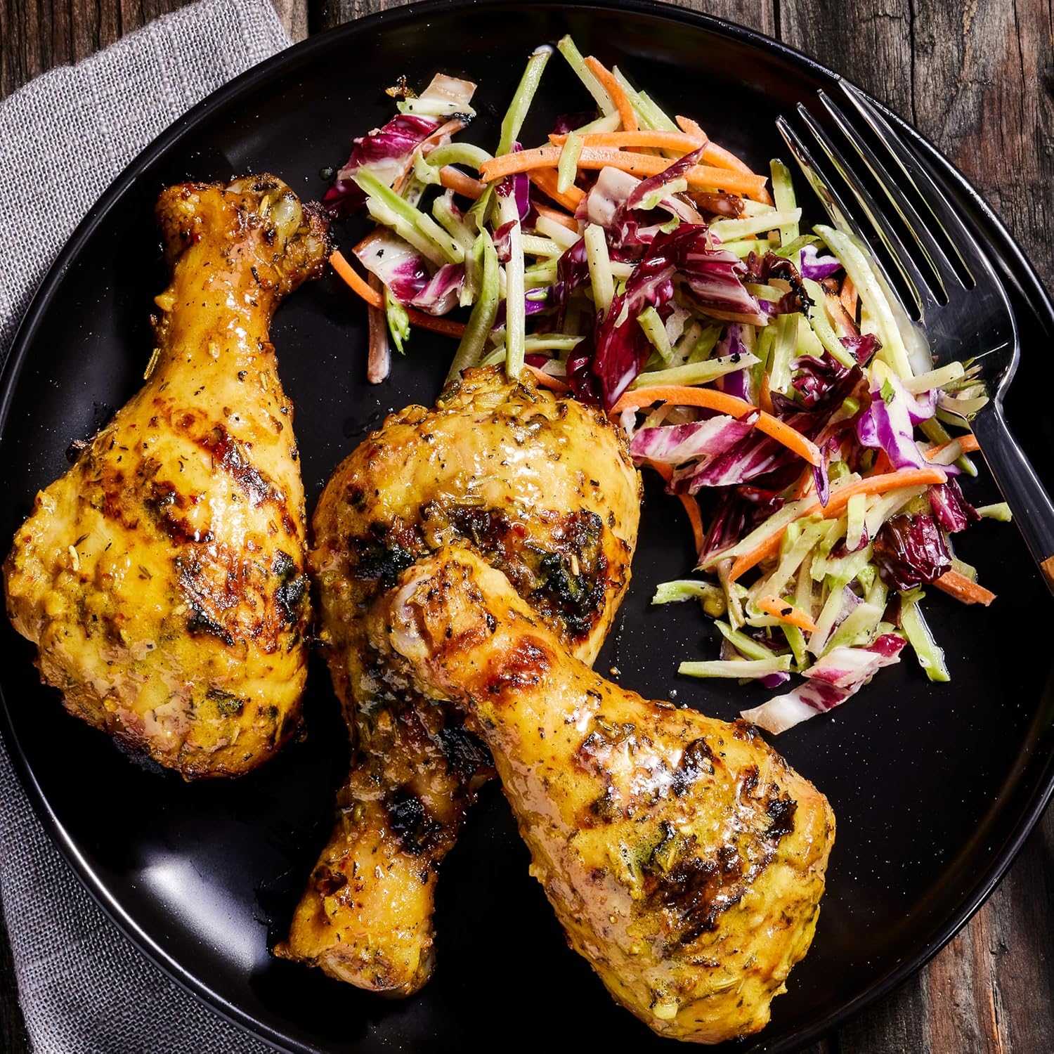 Two roasted chicken drumsticks on a black plate with a side of coleslaw.