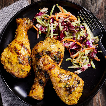 Two roasted chicken drumsticks on a black plate with a side of coleslaw.