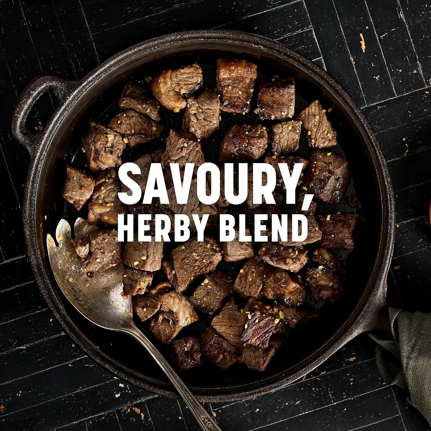 Savory spiced meat pieces seasoned with a herb blend - Club House La Grille Dill Pickle Seasoning in a cast iron skillet with a spoon on a dark surface