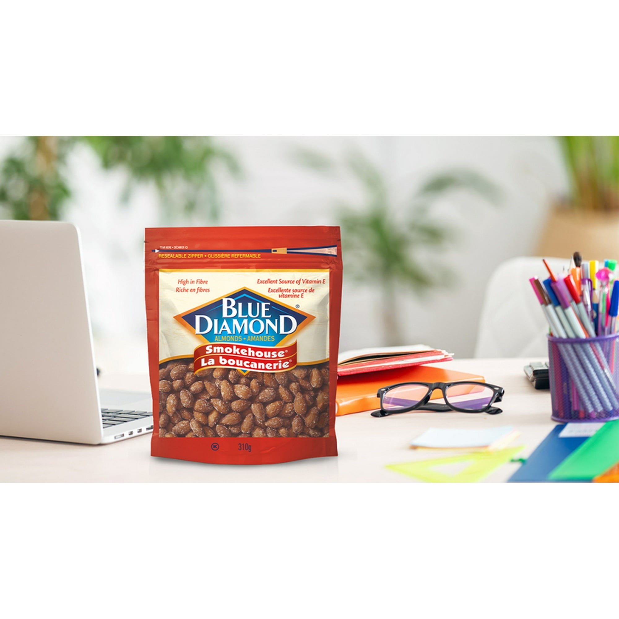 Blue Diamond Smokehouse almonds package on a desk with a laptop and stationery.