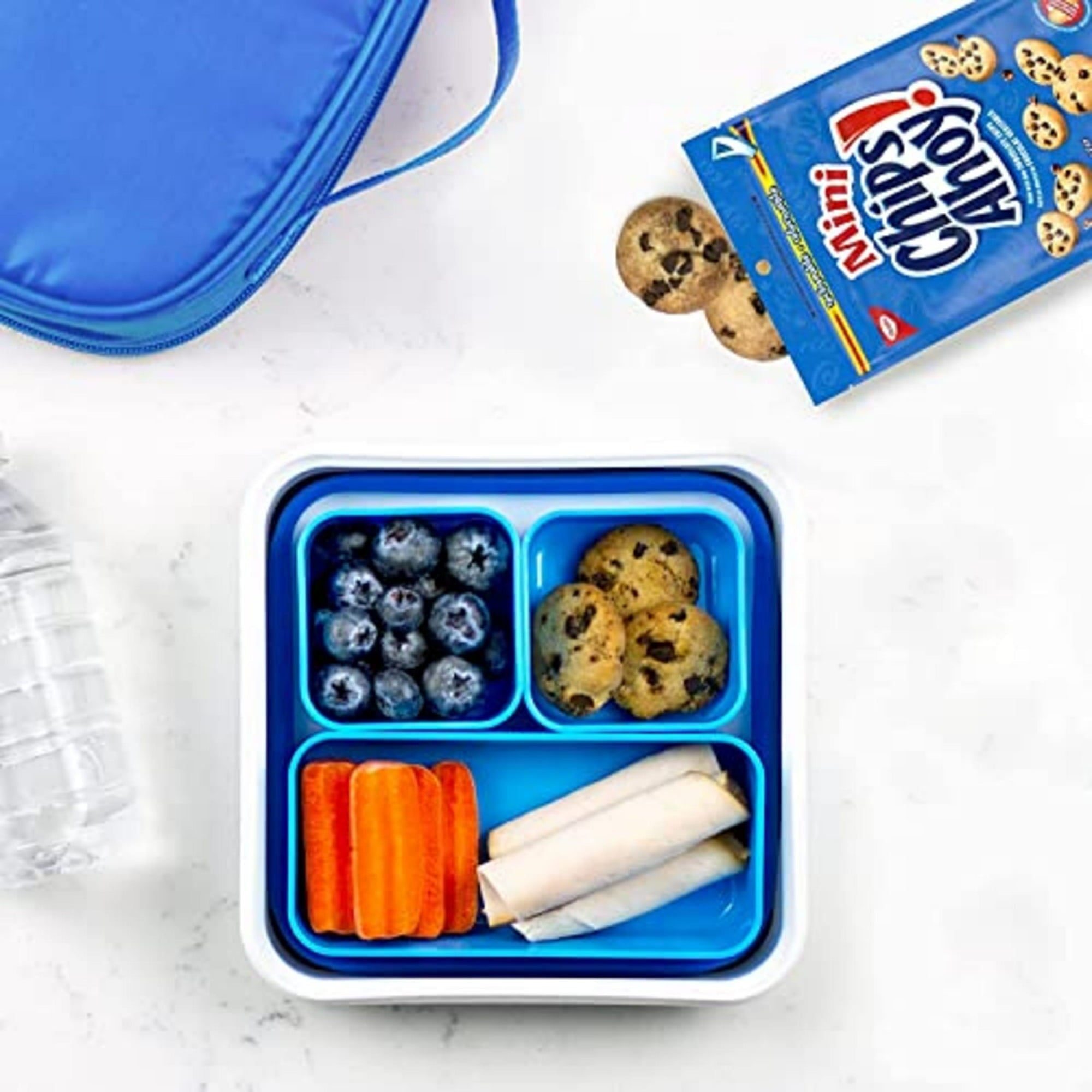 Blue bento box with compartments containing carrots, blueberries, and cookies on a white surface.