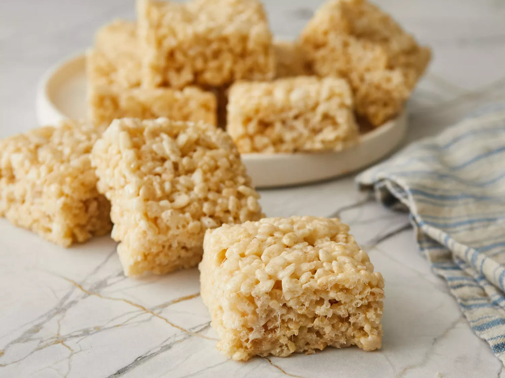 Rice krispie treats on a marble surface with a plate in the background