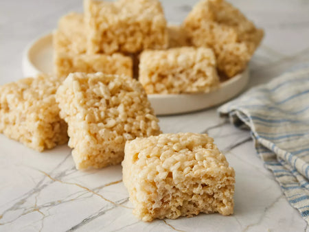 Rice krispie treats on a marble surface with a plate in the background