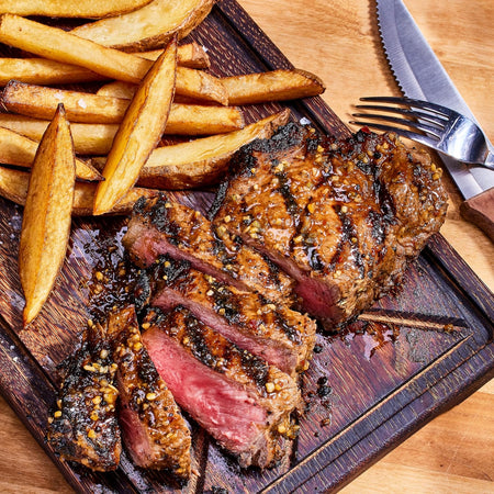 Grilled steak with fries on a wooden cutting board