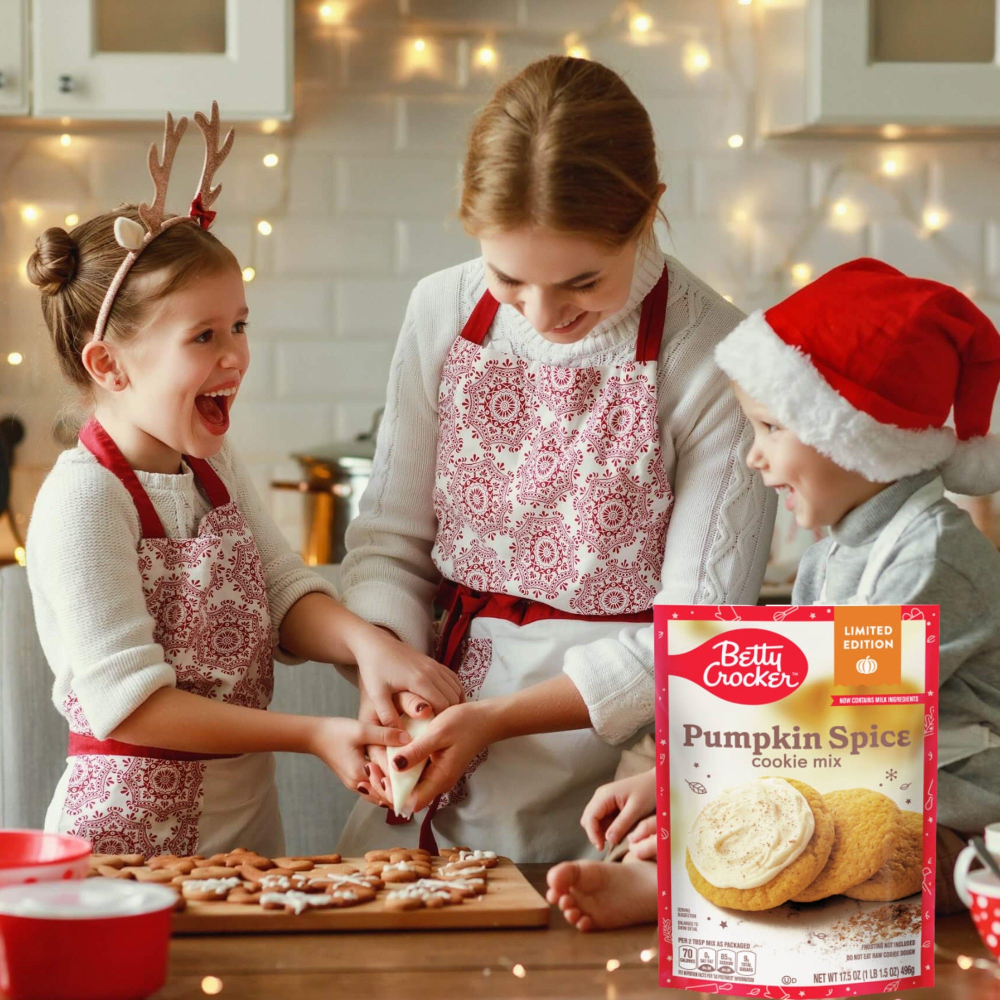 An adult and two children decorating cookies beside a Betty Crocker Pumpkin Spice Cookie Mix pouch in a festive kitchen.