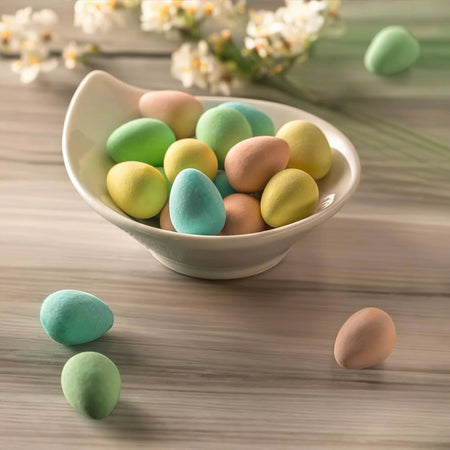 Pastel-colored Easter eggs in a bowl on a wooden surface with flowers in the background