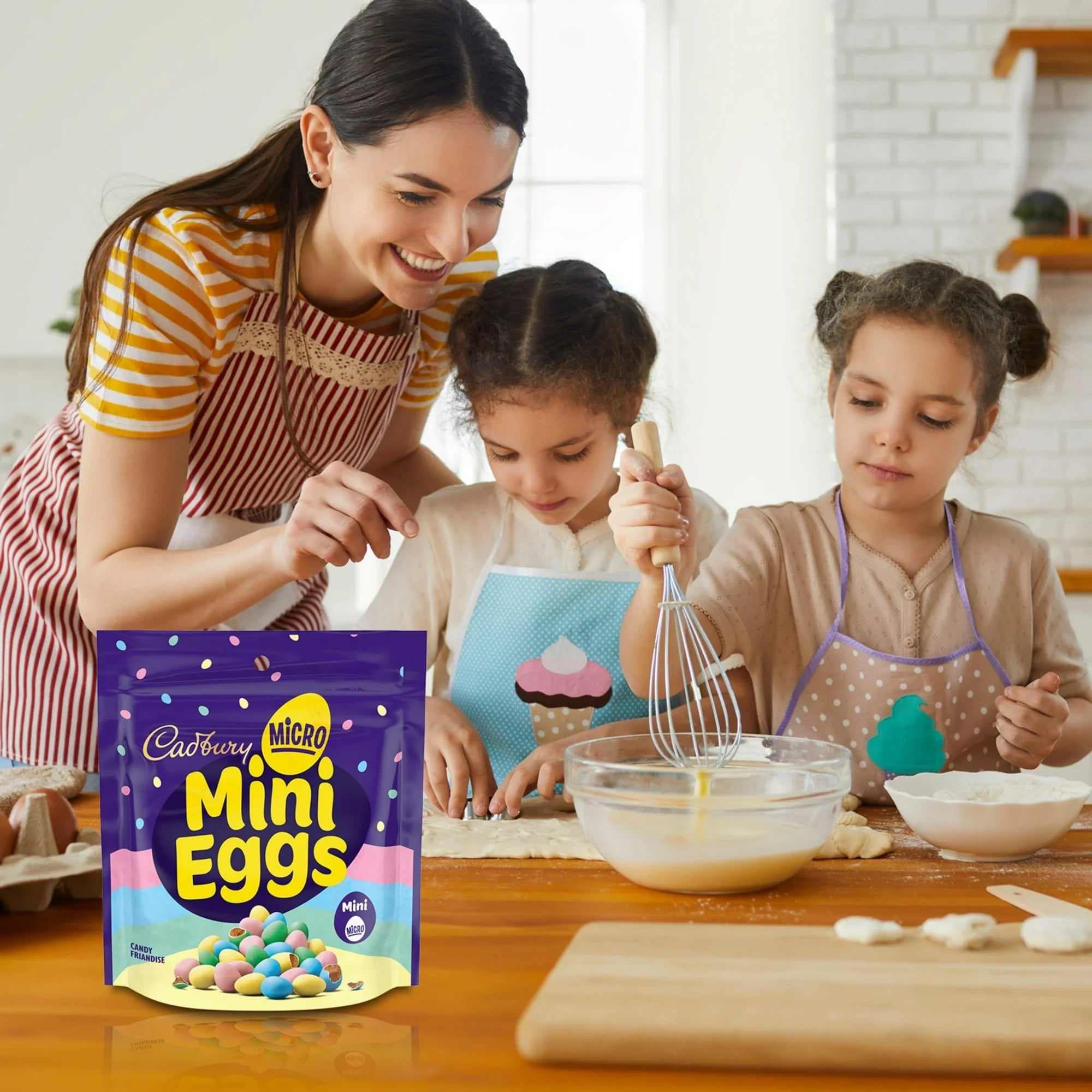 Woman and two children in a kitchen with Cadbury Micro Mini Eggs packaging.