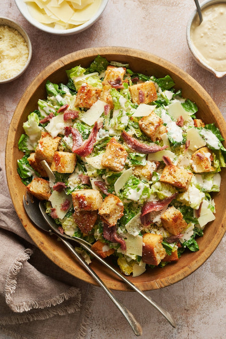 Caesar salad with two spoons in a wooden bowl on a beige cloth