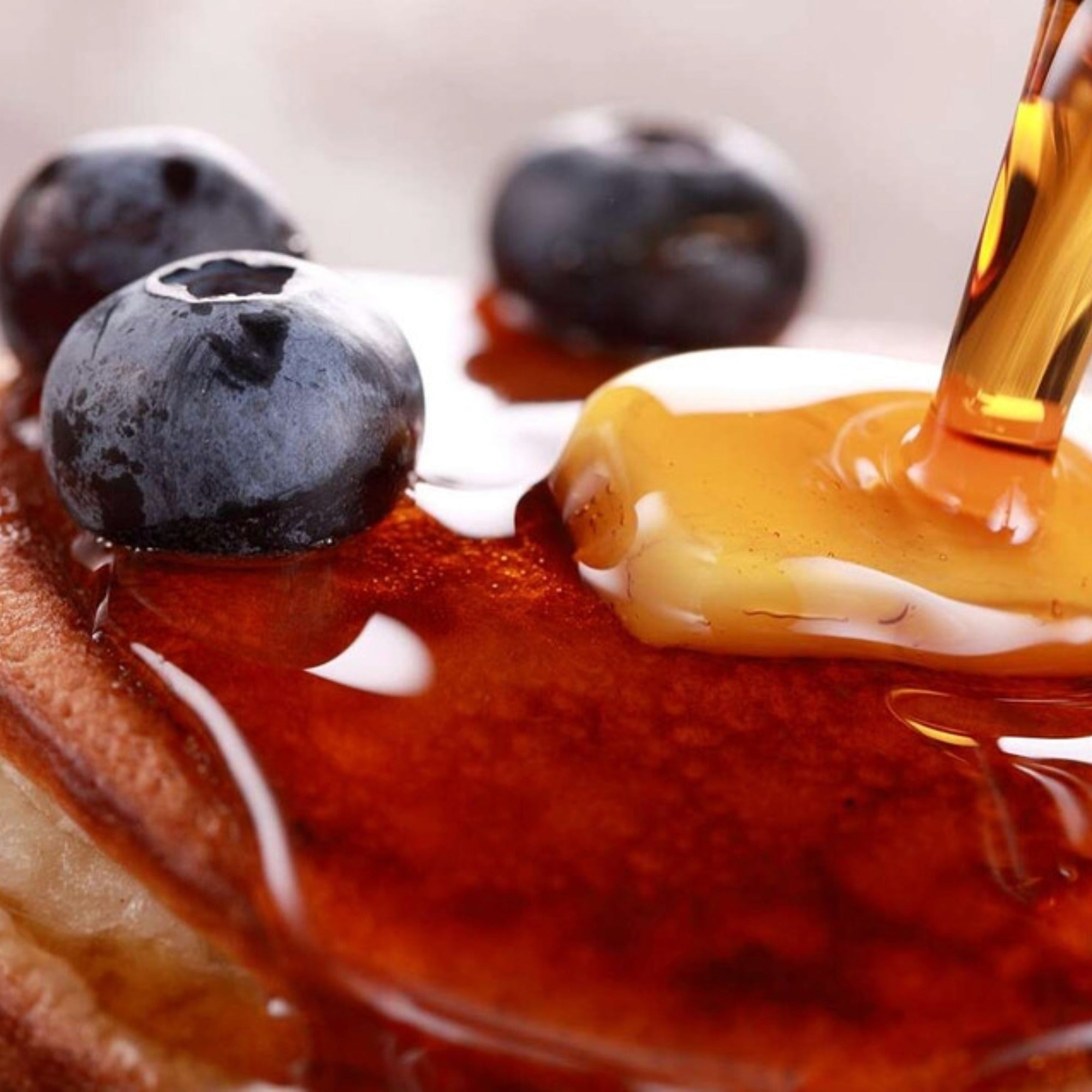 Maple syrup poured over a stack of pancakes topped with blueberries and butter.
