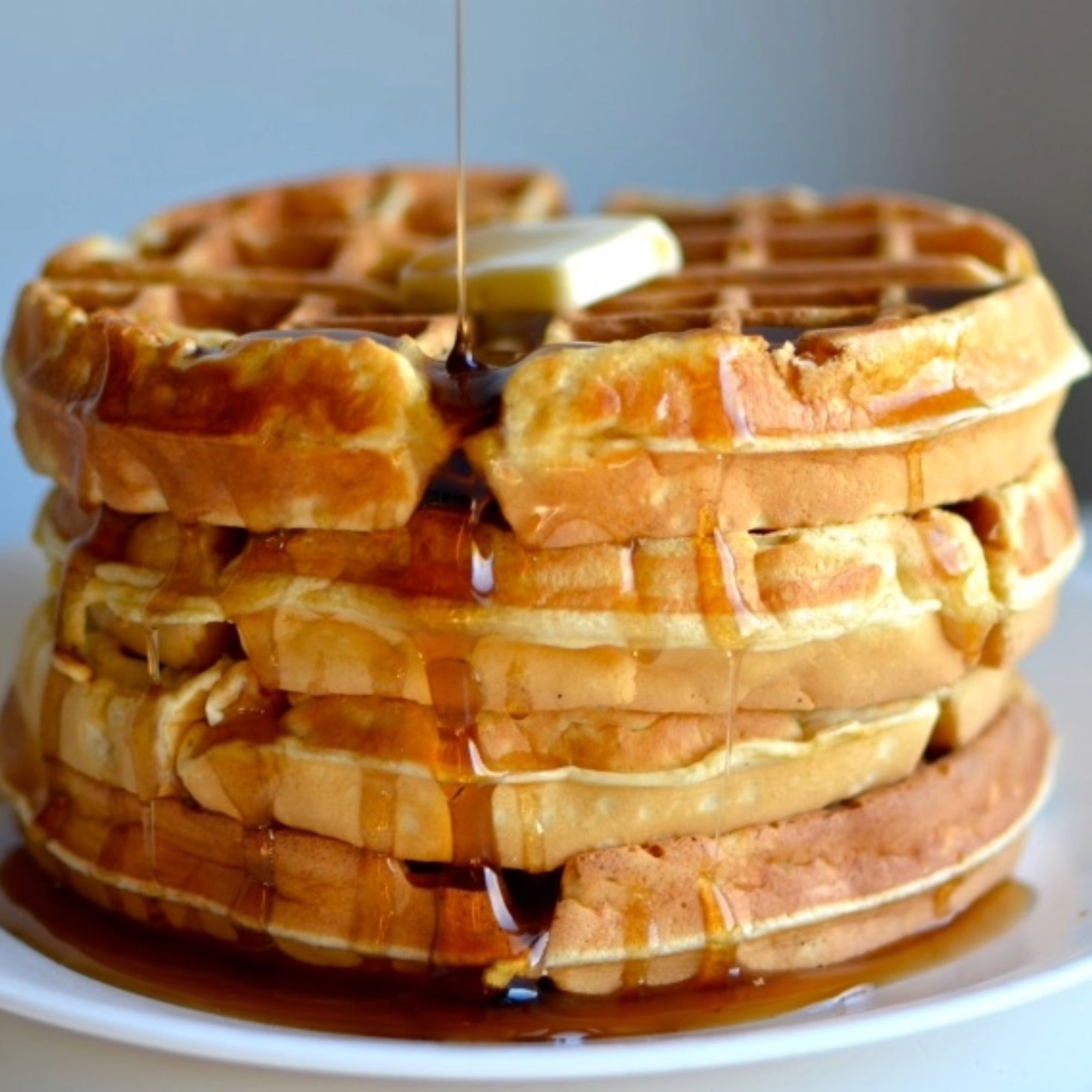 Syrup poured over a stack of waffles topped with butter.