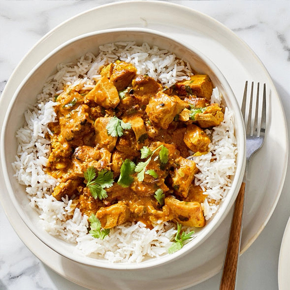 Bowl of chicken curry with rice on a marble surface