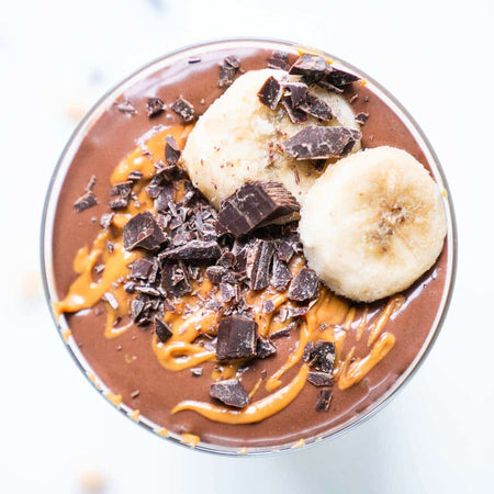 Chocolate smoothie bowl with banana slices and chocolate chunks on a white background