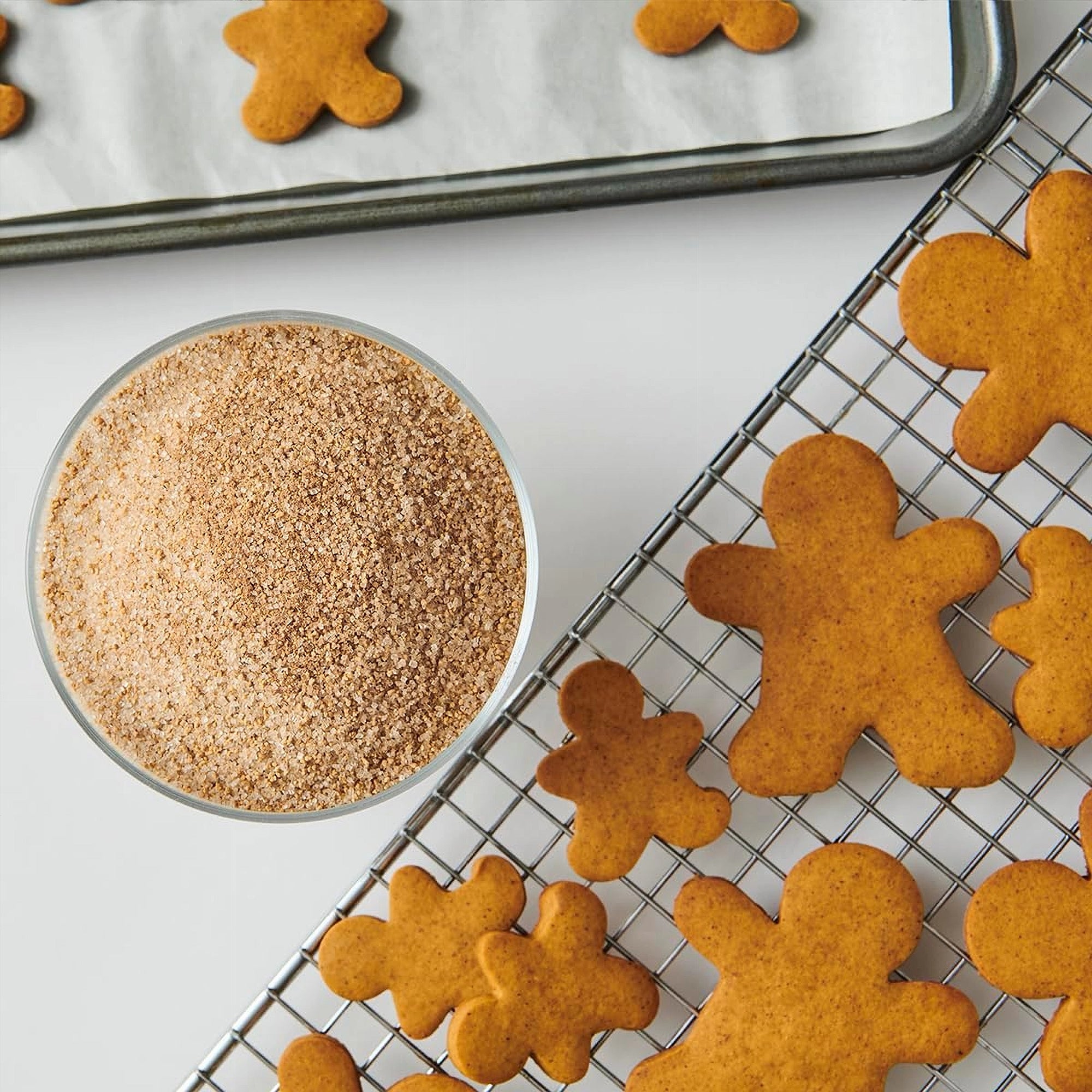 Baked gingerbread men on a cooling rack with a bowl of brown sugar.