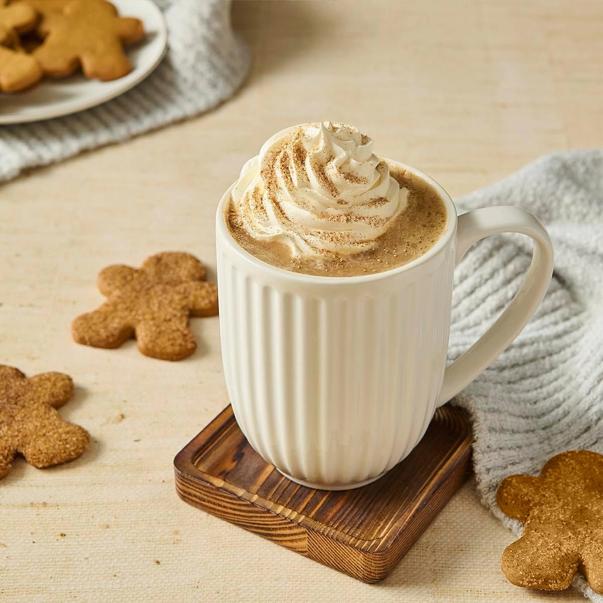 White mug with a creamy beverage and whipped cream, surrounded by gingerbread cookies on a wooden surface.