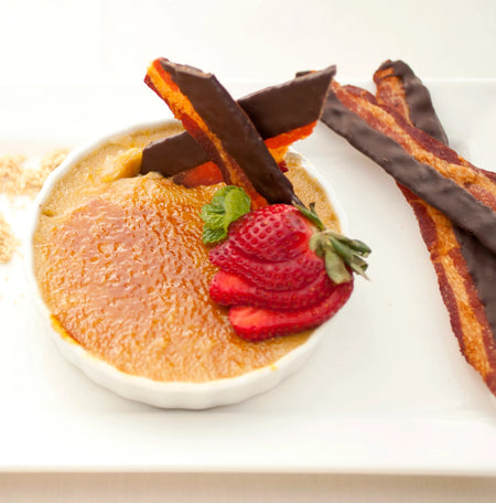 Dessert with creme brèle, chocolate-wrapped strawberries, and a strawberry on a white plate.