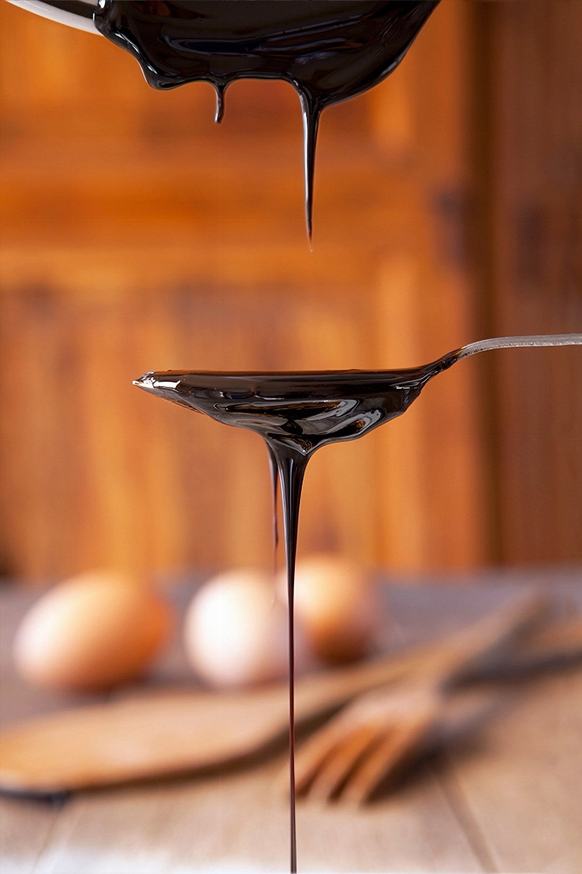 Molasses dripping from a spoon with a wooden background with eggs and cooking spoons on a table