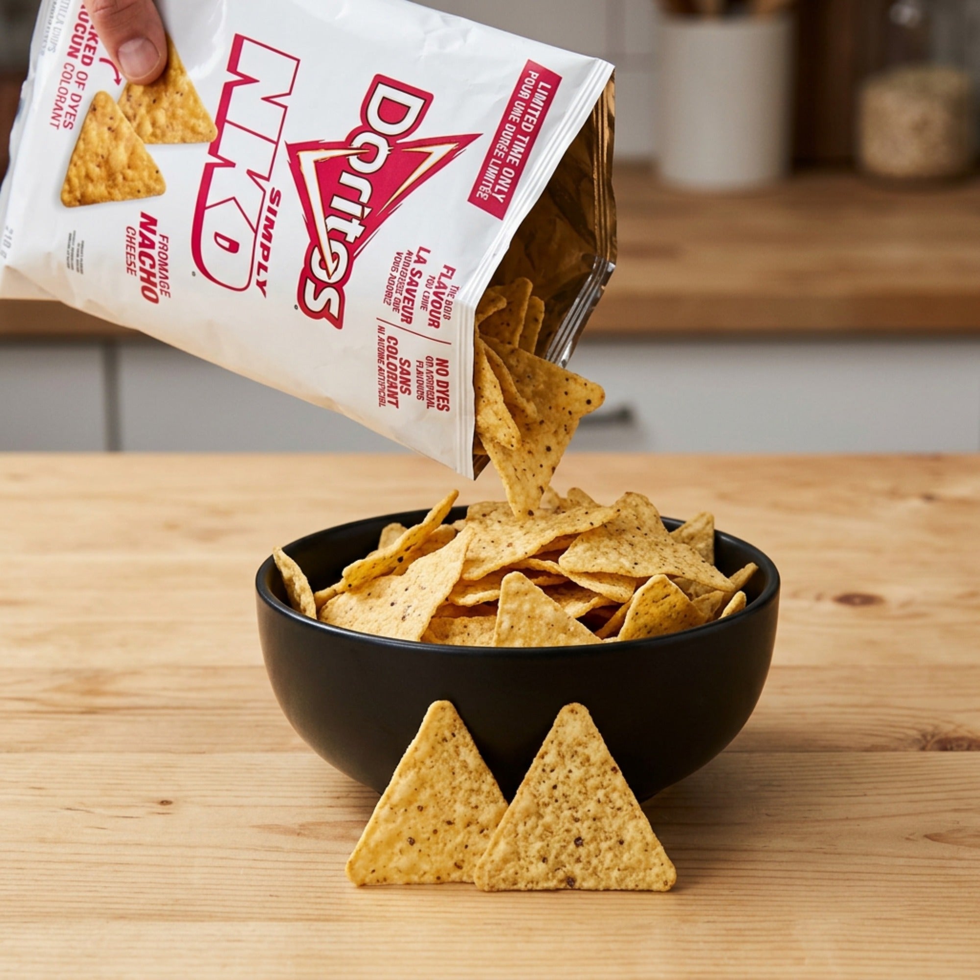 Doritos Simply NKD Nacho Cheese tortilla chips being poured from the bag into a black bowl on a wooden counter.