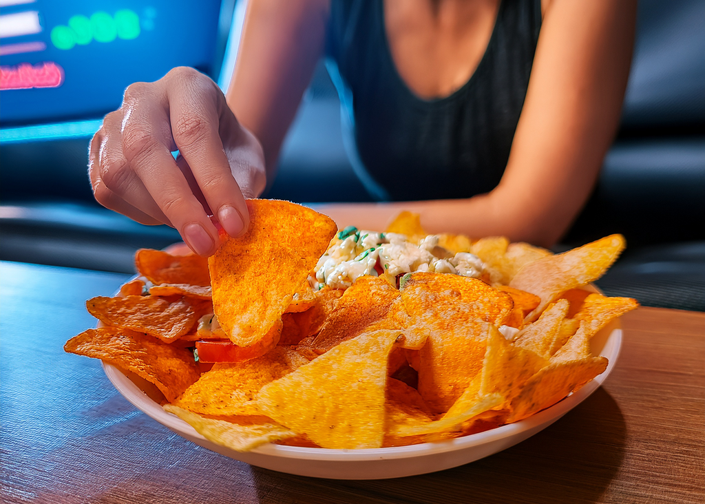 Person picking up a tortilla chip from a plate of nachos on a table.