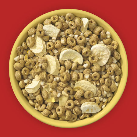 Yellow bowl filled with a mix of cereal and sliced bananas on a red background