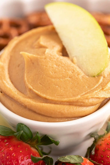 Peanut butter dip with an apple slice and strawberries in a white bowl.