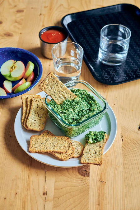 Boulangerie Grissol Melba Toast Sourdough Flavor with a spinach on a white plate with apples and water on a wooden table