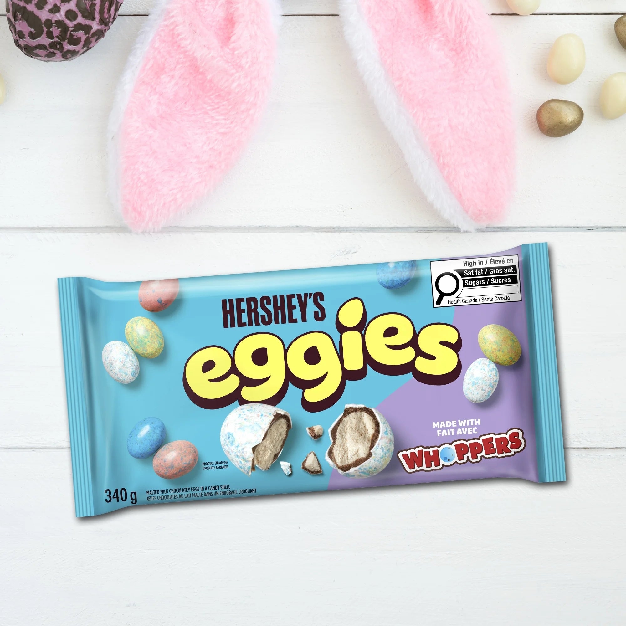 Hershey's Eggies candy package on a white wooden surface with Easter-themed elements.