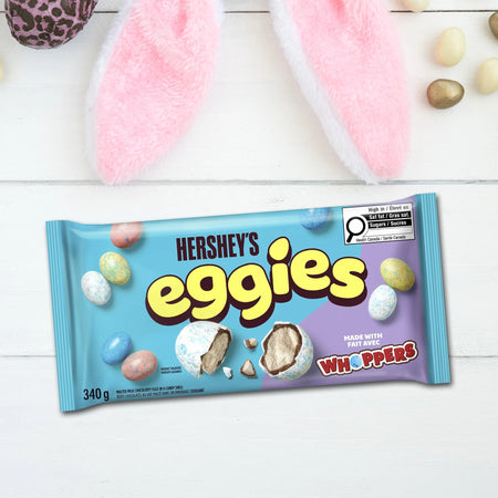 Hershey's Eggies candy package on a white wooden surface with Easter-themed elements.