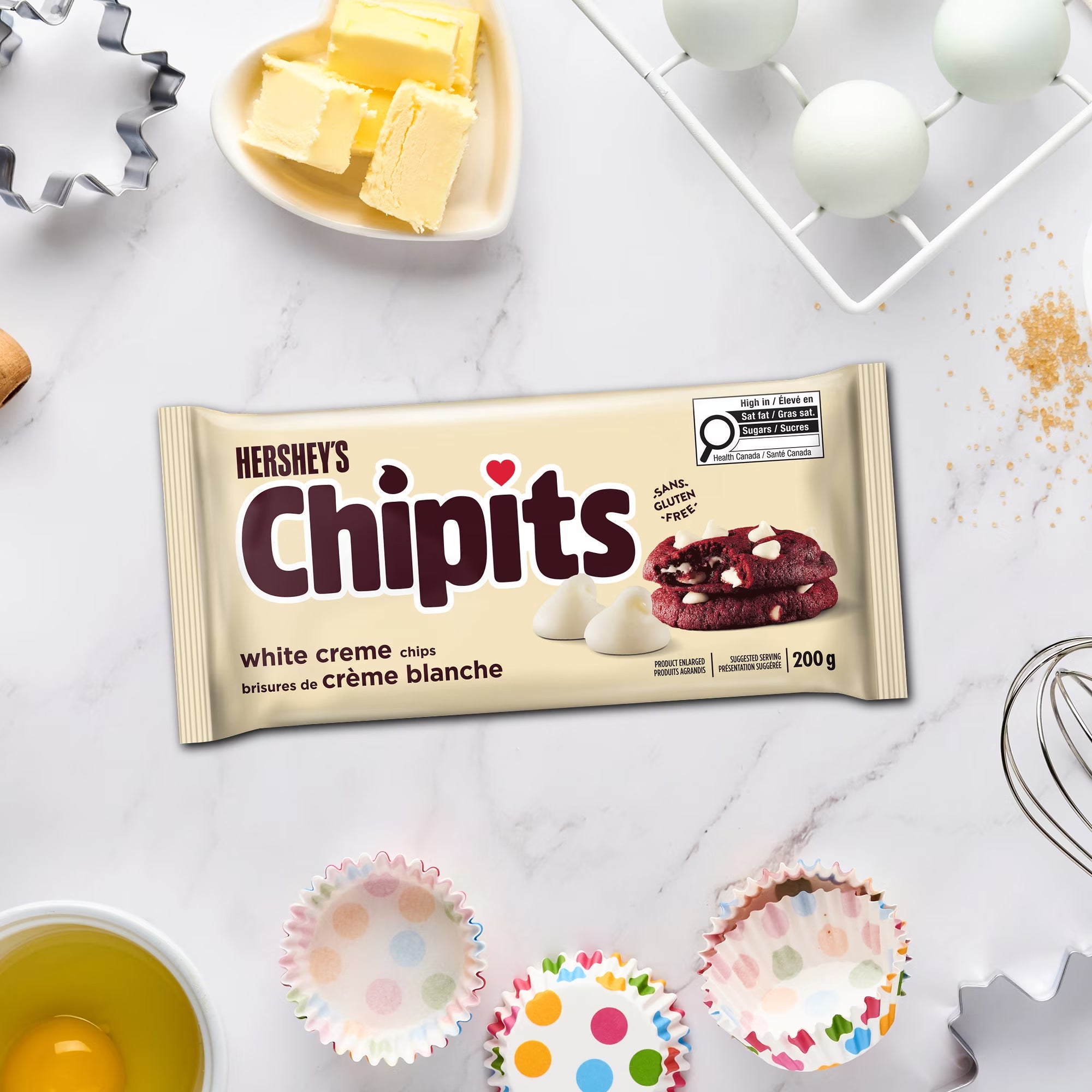 Hershey’s CHIPITS White Creme Chips package surrounded by eggs, butter, cupcake liners, and baking tools.