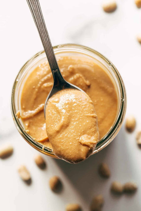 Jar of natural smooth peanut butter with a spoonful of peanut butter on a light background