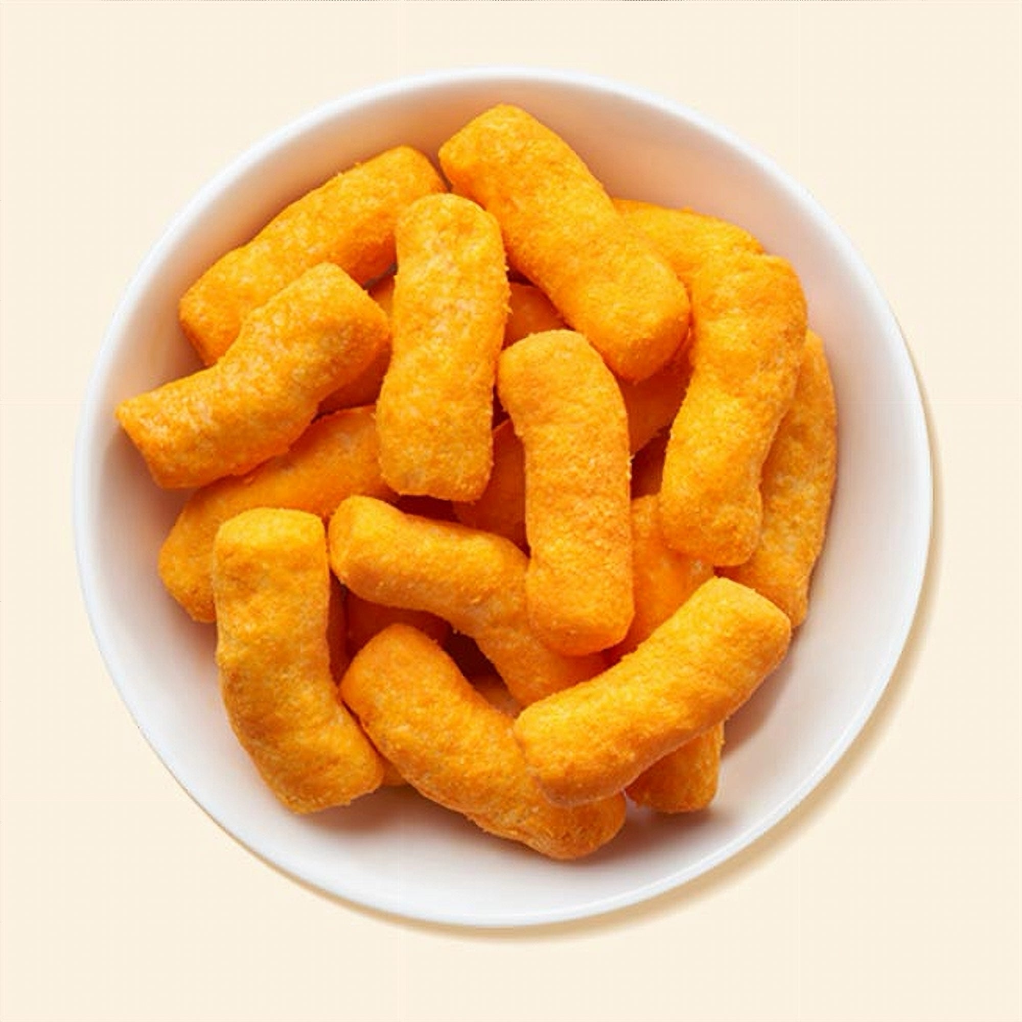 White bowl filled with orange cheese puffs on a light beige background